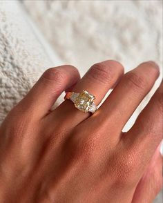 a woman's hand with a yellow diamond ring on her left hand and a white towel in the background