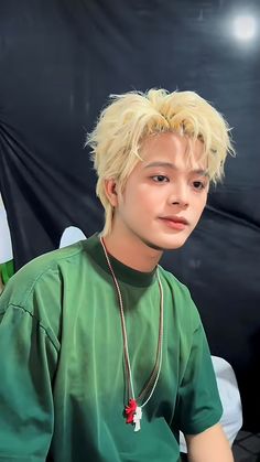 a young man with blonde hair wearing a green t - shirt and silver chain necklace