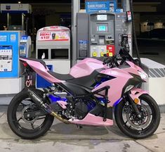 a pink motorcycle parked in front of a gas pump