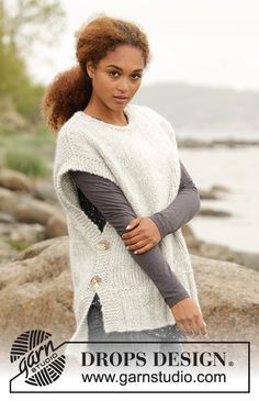 a woman standing on top of a rock next to the ocean wearing a white sweater