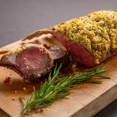 a piece of meat on a wooden cutting board with herbs and seasoning next to it