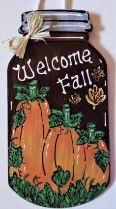 a welcome fall sign with pumpkins painted on the front and sides, hanging from a hook