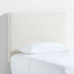 a bed with white sheets and pillows on top of it's headboard, against a wall