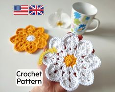 two crocheted flowers sitting on top of a table next to a coffee cup