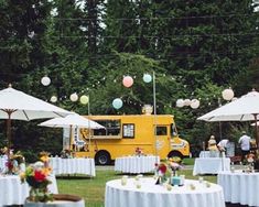 tables and umbrellas are set up outside for an outdoor wedding reception with food trucks in the background