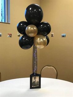 an arrangement of black and gold balloons in a vase on top of a white table