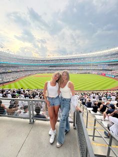 two women standing next to each other in front of a crowd at a baseball game