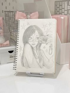 a notebook with a drawing of a girl holding a camera in front of her face