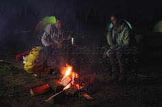 two people sitting around a campfire at night