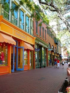 people are walking down the sidewalk in front of shops on a sunny day with colorful awnings