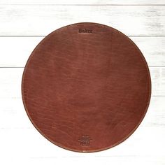 a round brown leather plate on a white wooden table with the word baker printed on it