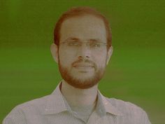 a man with glasses and beard standing in front of a green background