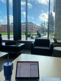 an open laptop computer sitting on top of a wooden table in front of large windows