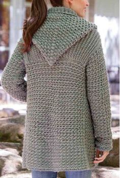 a woman wearing a green crocheted sweater and jeans standing in front of some rocks