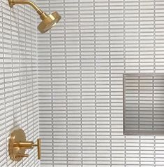 a white tiled bathroom with gold fixtures and square shower head in the corner, next to toilet paper dispenser