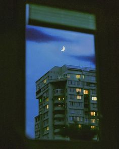 the moon is seen through an open window in a building at night with lights on