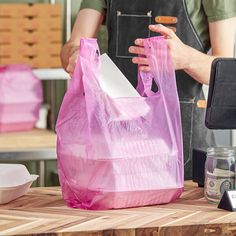 a person holding a pink shopping bag on top of a wooden table next to other items