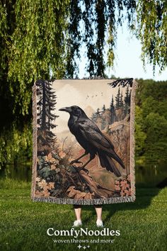 a black bird sitting on top of a lush green field next to a forest filled with trees