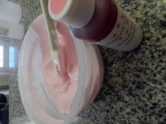 a person is holding a toothbrush in a container with pink stuff on the counter