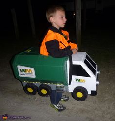 a young boy riding on the back of a green and white toy truck at night