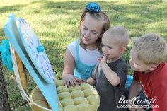 three children sitting on the ground looking at something in a basket that is shaped like a surfboard