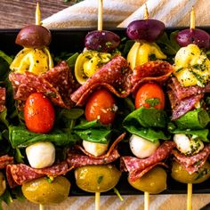 several skewers filled with meat, vegetables and olives on top of a wooden table