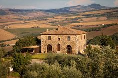 an old stone building in the middle of a field with trees and hills behind it