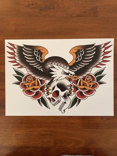 an eagle and skull with roses on it is sitting on a wooden table next to a pair of scissors