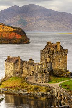 an old castle sitting on top of a small island next to the ocean with mountains in the background