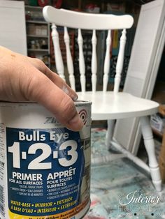 a person holding a can of paint in front of a white chair with the words bulls eye 12 - 23 primer aprret