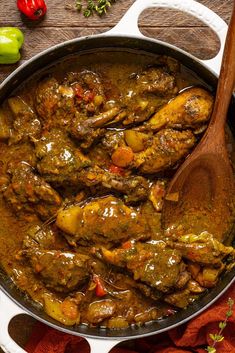 a large pot filled with meat and vegetables on top of a wooden table next to peppers