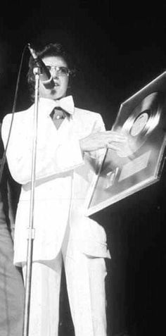 a man in a white suit and tie holding a microphone