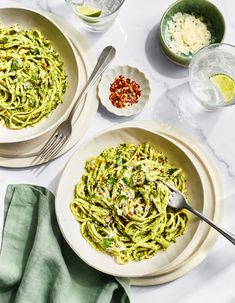 two white bowls filled with green pasta on top of a table