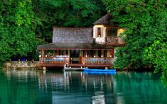 a house sitting on top of a lake surrounded by green trees next to a forest