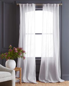 a white chair sitting next to a window with sheer curtains on the windowsills