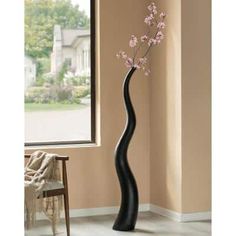 a tall black vase with pink flowers in it on a table next to a window