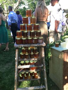 people are standing around and looking at some jars on a wooden stand in the grass