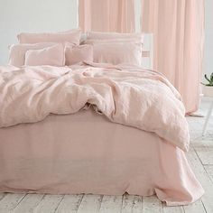 a bed with pink sheets and pillows in a white room next to a potted plant