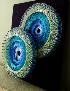 two blue and green peacock feathers on a black canvas mounted to a wall in a living room