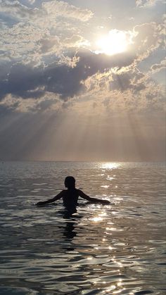 a person is swimming in the ocean with sun shining down on them and some clouds