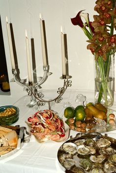 an arrangement of food on a table with candles and flowers in vases next to it