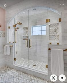 a bathroom with white tile and gold trim on the shower door, windows, and towel racks