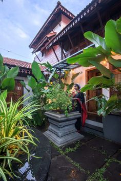 a woman standing in front of a potted plant next to a tall white building