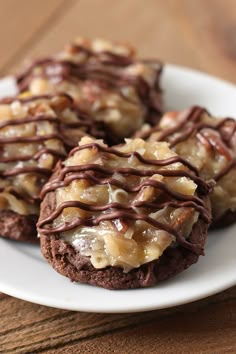 three cookies covered in chocolate drizzled with nuts on a white plate sitting on a wooden table