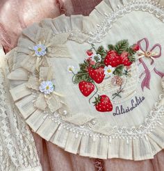 an embroidered heart with strawberries on it and ribbon around the edges, is displayed