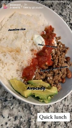 a white bowl filled with rice, meat and avocado on top of a table