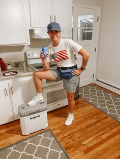 a woman sitting on top of a cooler in a kitchen next to a stove and refrigerator