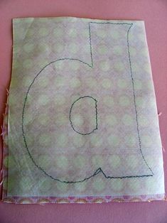 a piece of fabric with the letter b on it is laying on a pink surface