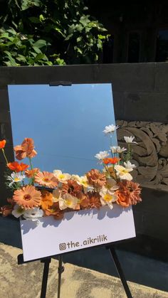 an easel with flowers on it sitting in front of a sign that says the alkirlix