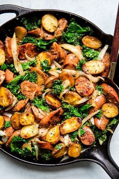 a skillet filled with potatoes, broccoli and other vegetables on top of a table